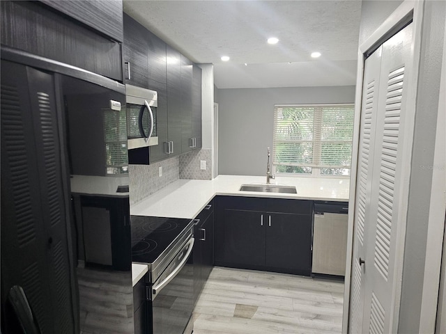 kitchen with a textured ceiling, appliances with stainless steel finishes, decorative backsplash, sink, and light hardwood / wood-style floors