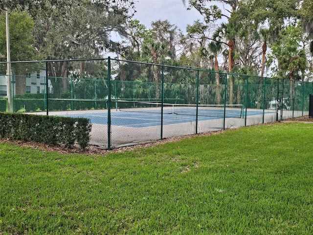 view of tennis court featuring fence and a yard