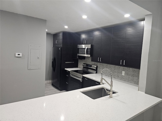 kitchen featuring decorative backsplash, appliances with stainless steel finishes, a sink, dark cabinetry, and a peninsula