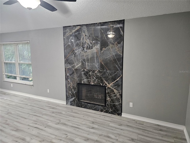 room details featuring a textured ceiling, a fireplace, wood finished floors, a ceiling fan, and baseboards