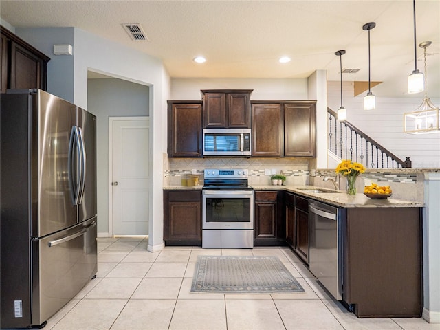 kitchen featuring light stone countertops, light tile patterned floors, sink, decorative light fixtures, and stainless steel appliances