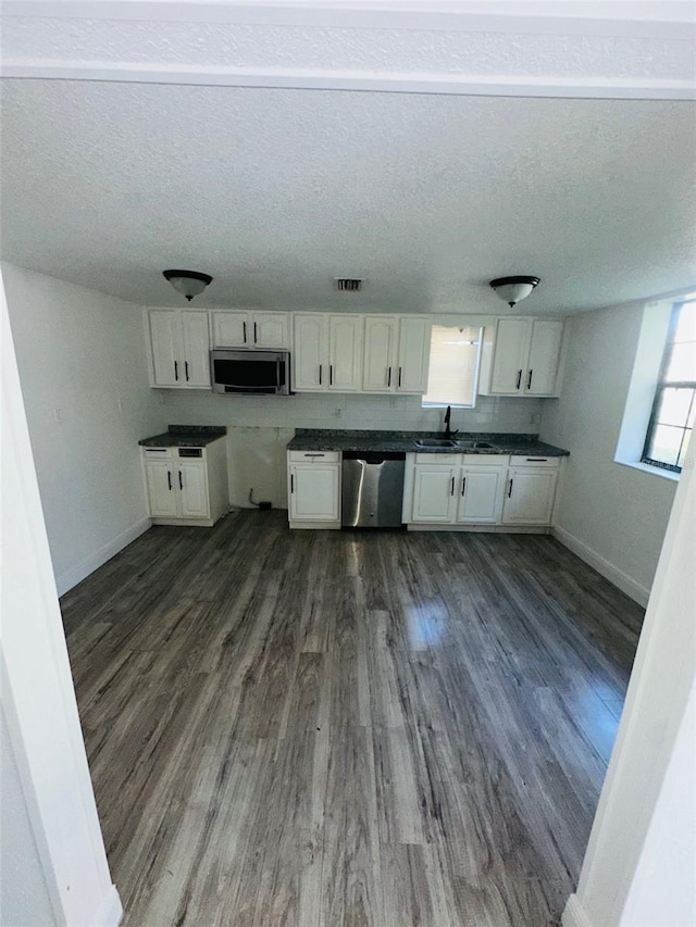 kitchen with a textured ceiling, appliances with stainless steel finishes, dark wood-type flooring, white cabinetry, and sink