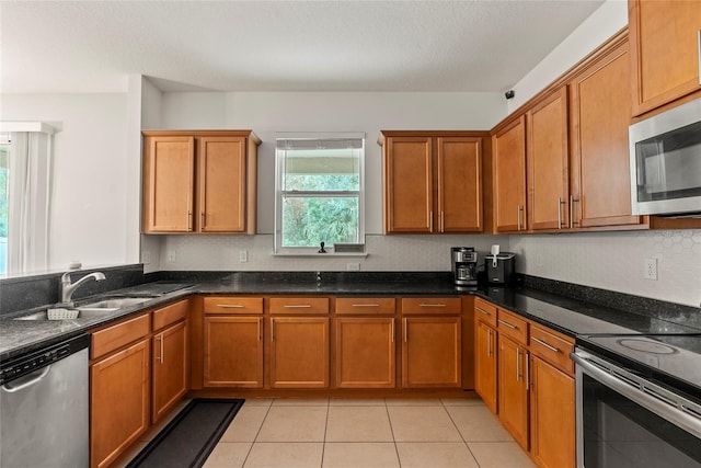 kitchen with sink, dark stone countertops, light tile patterned floors, and appliances with stainless steel finishes