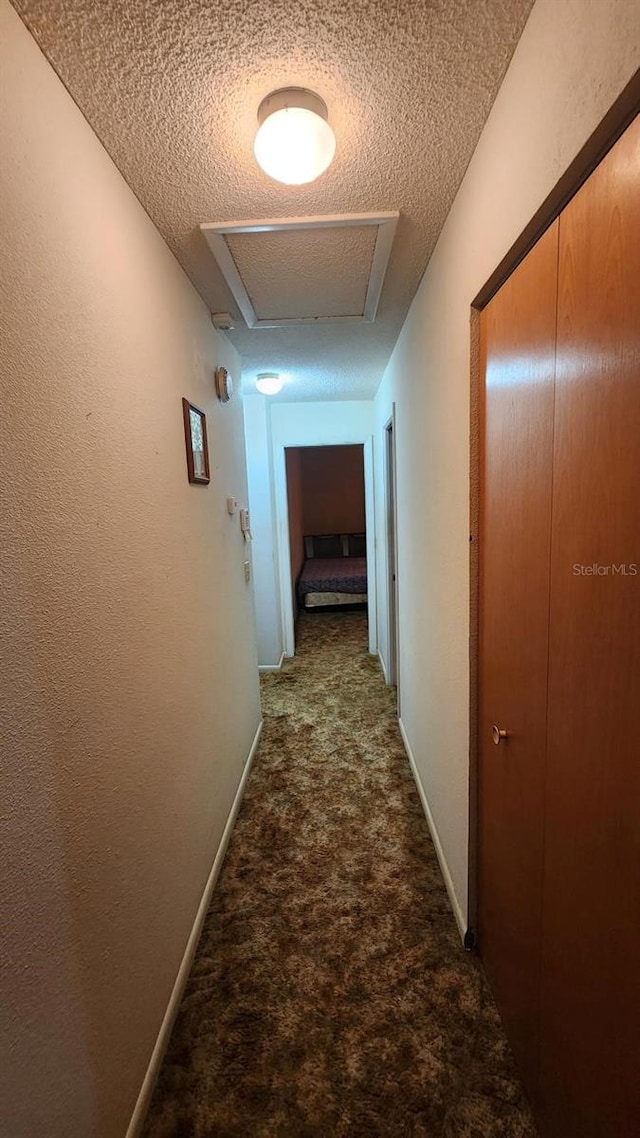 hallway featuring a textured ceiling and dark carpet