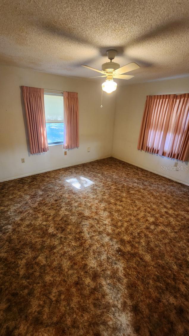 carpeted spare room with a textured ceiling and ceiling fan