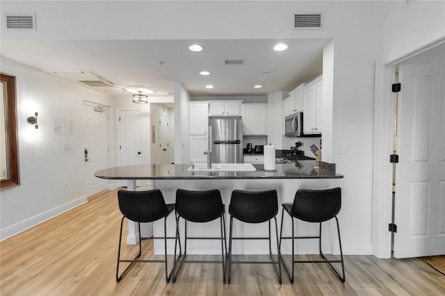 kitchen featuring light hardwood / wood-style flooring, white cabinetry, a kitchen breakfast bar, stainless steel appliances, and kitchen peninsula