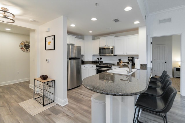 kitchen featuring a breakfast bar, sink, white cabinetry, dark stone counters, and stainless steel appliances