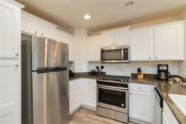 kitchen with stainless steel appliances, white cabinetry, light hardwood / wood-style floors, and dark stone counters