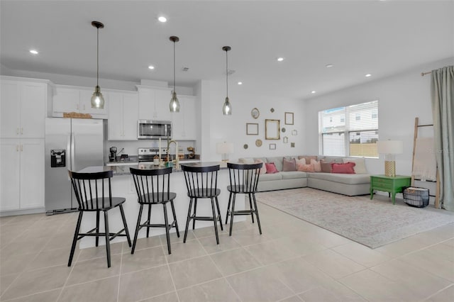 interior space with appliances with stainless steel finishes, white cabinetry, hanging light fixtures, light tile patterned flooring, and a breakfast bar area