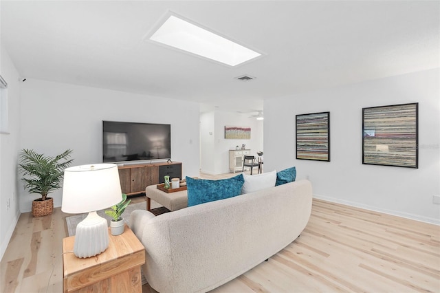 living room featuring a skylight, visible vents, light wood-style flooring, and baseboards