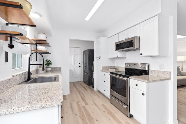 kitchen featuring light wood-style floors, appliances with stainless steel finishes, open shelves, and a sink