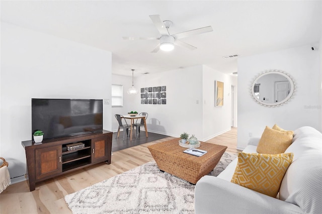 living room featuring light wood-style floors, ceiling fan, visible vents, and baseboards