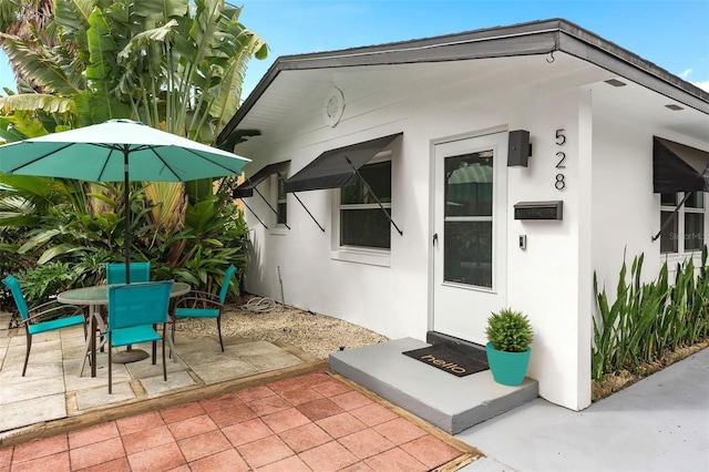 property entrance featuring stucco siding, outdoor dining space, and a patio area