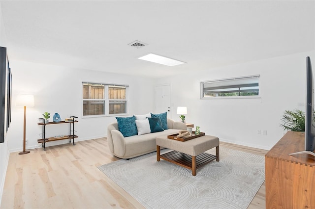 living room featuring a skylight, light wood-style flooring, visible vents, and baseboards