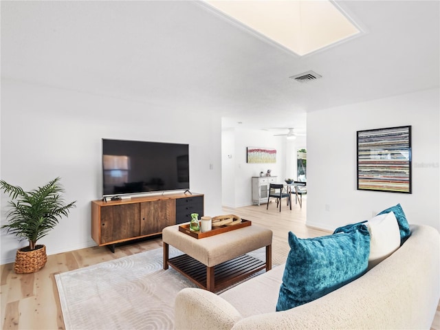 living room with baseboards, light wood finished floors, visible vents, and a ceiling fan