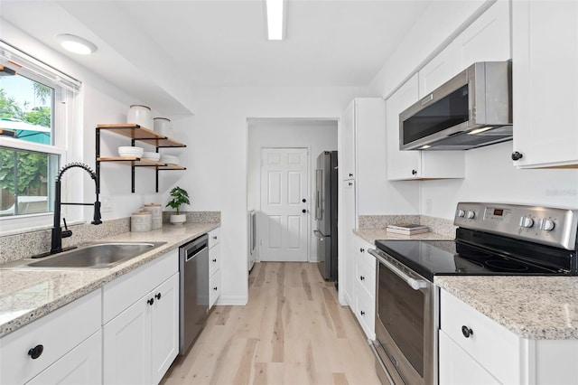 kitchen featuring light wood-style flooring, stainless steel appliances, white cabinetry, open shelves, and a sink