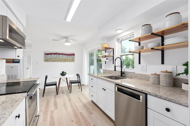 kitchen featuring light wood finished floors, open shelves, stainless steel appliances, white cabinetry, and a sink