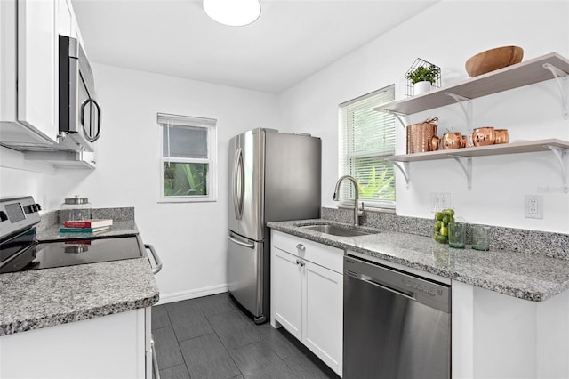 kitchen with baseboards, white cabinets, light stone counters, stainless steel appliances, and a sink