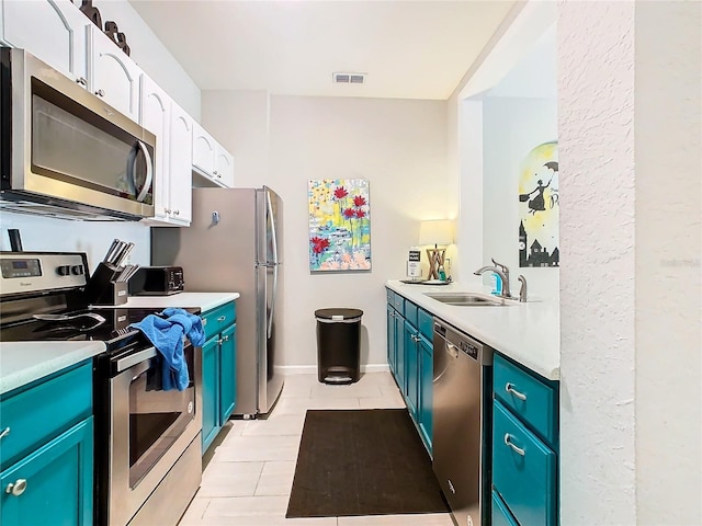 kitchen featuring sink, light tile patterned floors, appliances with stainless steel finishes, white cabinets, and blue cabinets