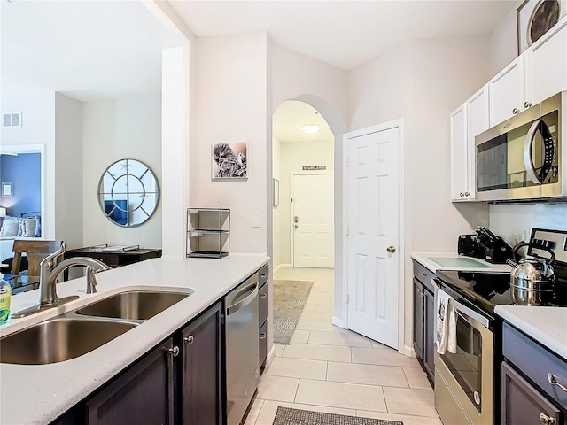 kitchen with appliances with stainless steel finishes, dark brown cabinetry, white cabinetry, sink, and light tile patterned floors