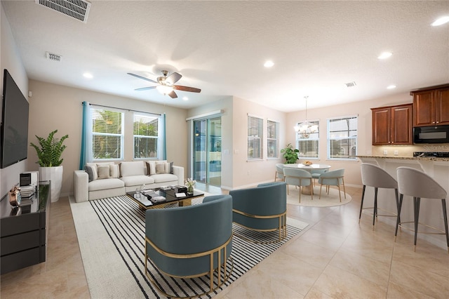 tiled living room with ceiling fan with notable chandelier and a healthy amount of sunlight