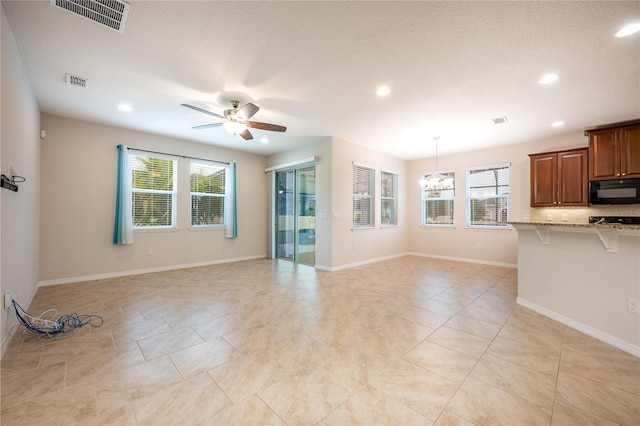 unfurnished living room with a healthy amount of sunlight, ceiling fan with notable chandelier, and a textured ceiling