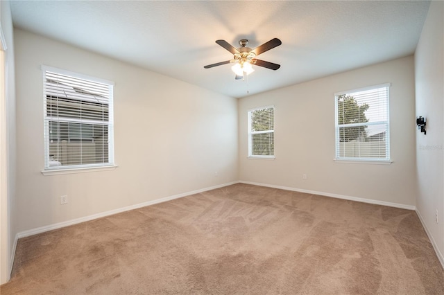 empty room featuring ceiling fan, light colored carpet, and a healthy amount of sunlight