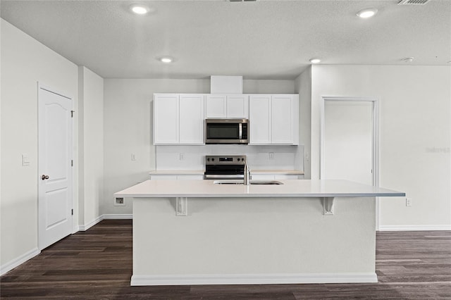 kitchen featuring dark wood-type flooring, white cabinets, appliances with stainless steel finishes, and a center island with sink