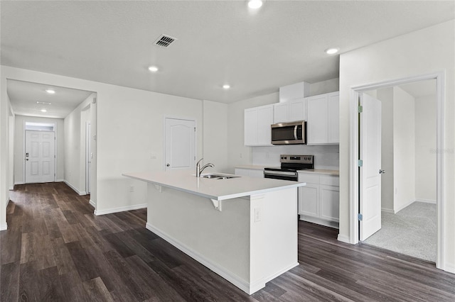 kitchen featuring dark wood-type flooring, appliances with stainless steel finishes, white cabinetry, and a kitchen island with sink