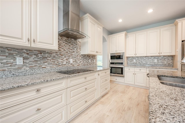 kitchen with light stone counters, backsplash, wall chimney range hood, and stainless steel appliances