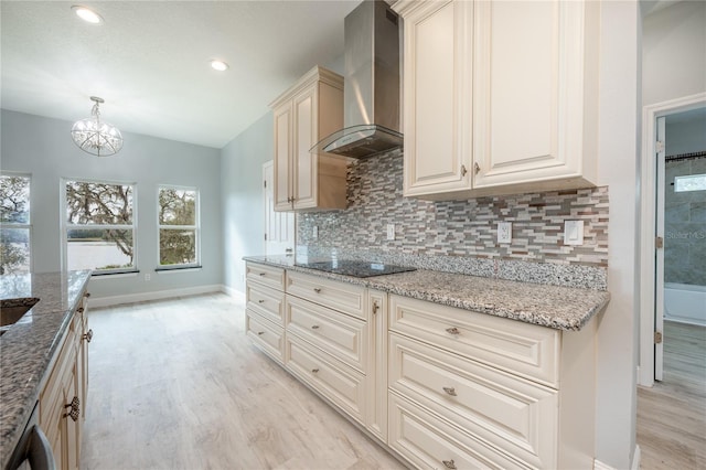 kitchen featuring decorative light fixtures, cream cabinetry, black electric stovetop, light stone counters, and wall chimney range hood