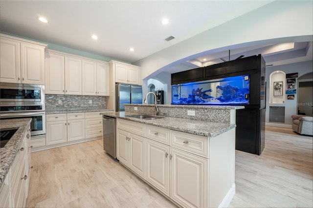 kitchen featuring appliances with stainless steel finishes, decorative backsplash, sink, light wood-type flooring, and an island with sink