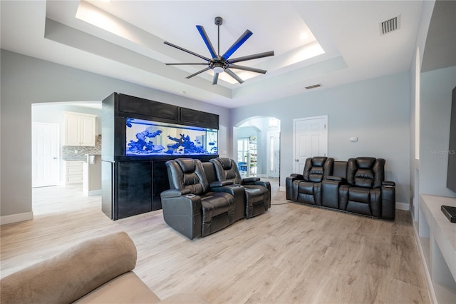 home theater room with ceiling fan, light hardwood / wood-style flooring, and a tray ceiling