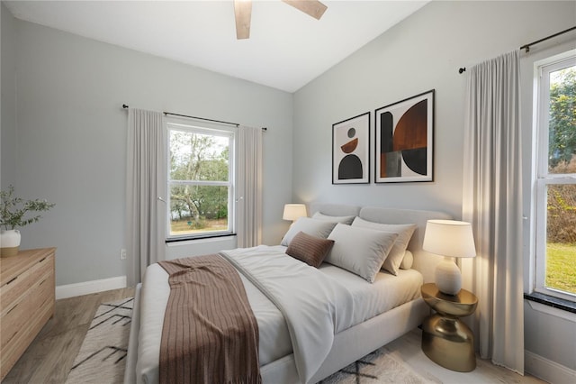 bedroom featuring ceiling fan, multiple windows, vaulted ceiling, and light wood-type flooring