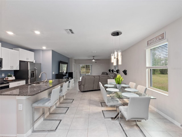 kitchen with white cabinets, dark stone countertops, an island with sink, hanging light fixtures, and a breakfast bar