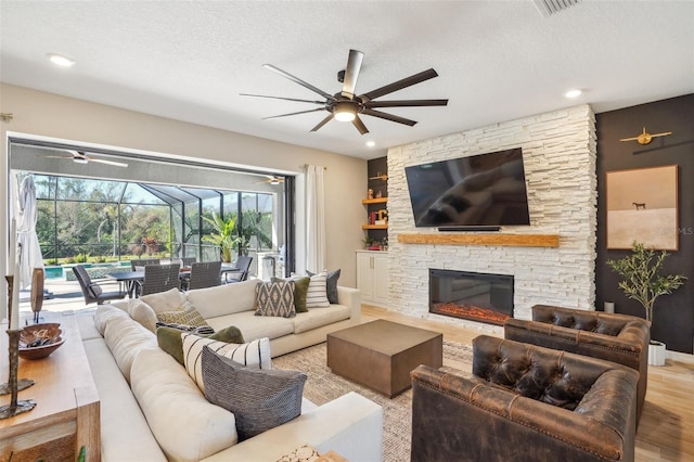 living room featuring ceiling fan, plenty of natural light, a fireplace, and a textured ceiling