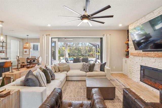 living room with ceiling fan, a stone fireplace, light hardwood / wood-style flooring, and a textured ceiling