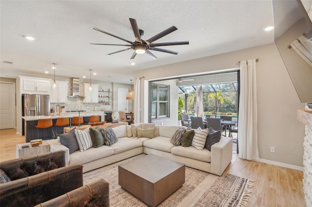 living room with a textured ceiling, a fireplace, ceiling fan, and light hardwood / wood-style flooring