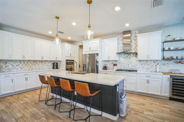 kitchen with wall chimney range hood, pendant lighting, stainless steel appliances, beverage cooler, and white cabinets