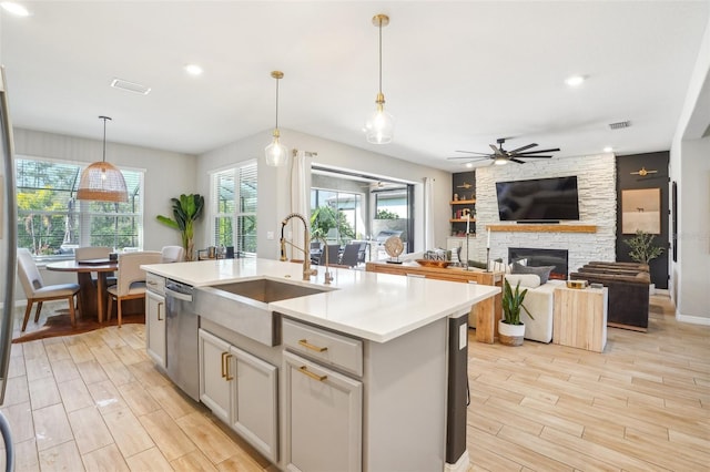 kitchen featuring sink, a kitchen island with sink, hanging light fixtures, a fireplace, and stainless steel dishwasher