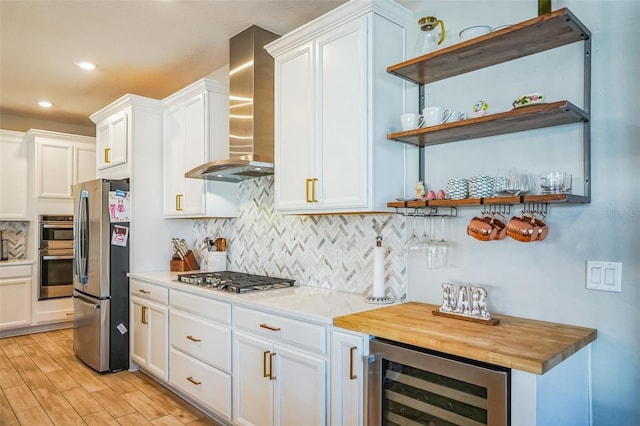 kitchen with wine cooler, appliances with stainless steel finishes, wall chimney range hood, light hardwood / wood-style floors, and white cabinets