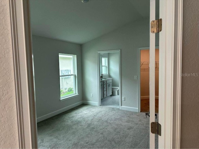 unfurnished bedroom with a walk in closet, lofted ceiling, sink, light colored carpet, and ensuite bathroom