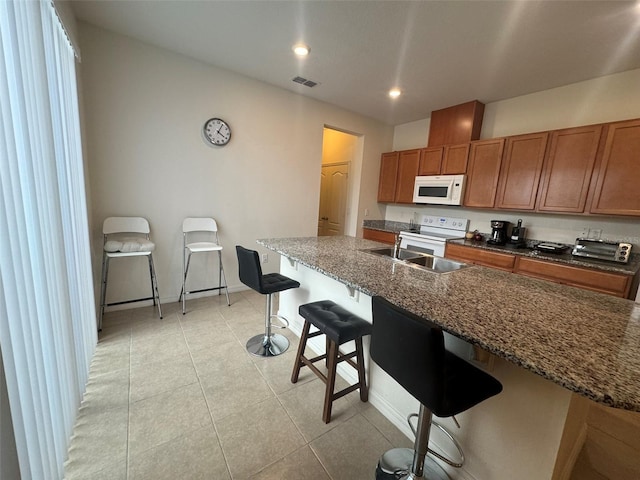 kitchen featuring sink, white appliances, light tile patterned floors, a breakfast bar, and a center island with sink