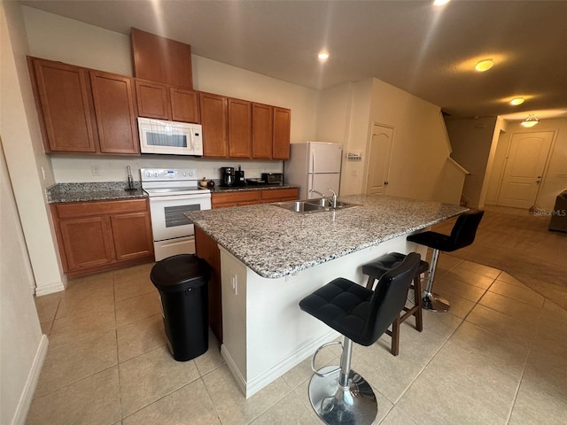 kitchen featuring a breakfast bar, sink, a center island with sink, light tile patterned floors, and white appliances