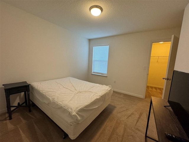 bedroom with a walk in closet, a textured ceiling, a closet, and dark colored carpet