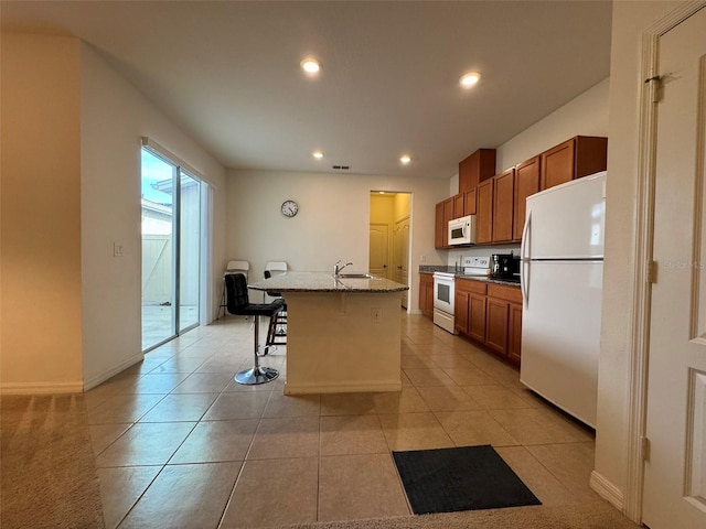 kitchen featuring sink, a kitchen breakfast bar, a kitchen island with sink, light stone countertops, and white appliances