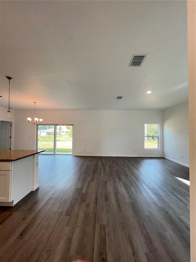 unfurnished living room featuring dark wood-type flooring, a chandelier, and a textured ceiling