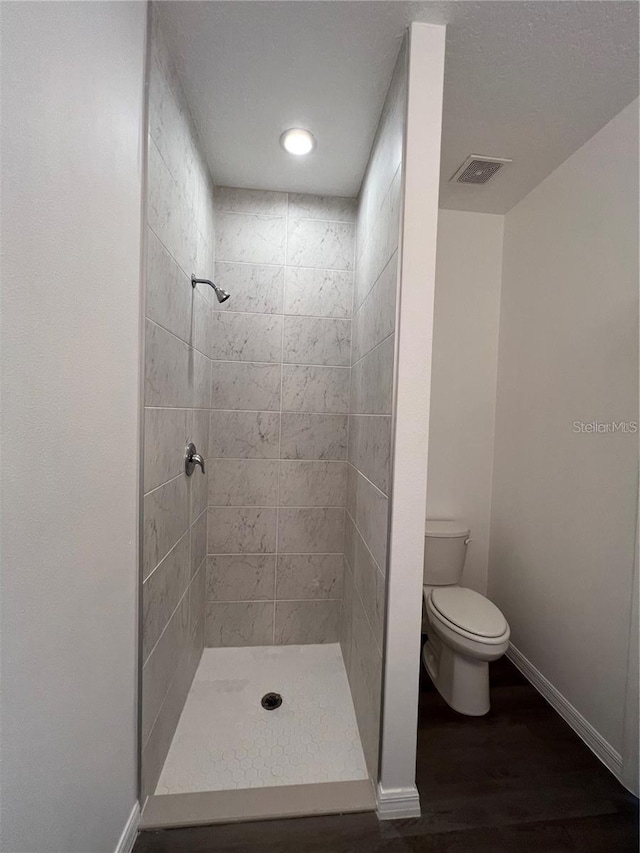 bathroom with toilet, tiled shower, and hardwood / wood-style flooring