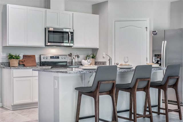 kitchen featuring a kitchen bar, white cabinets, stainless steel appliances, and light tile patterned flooring