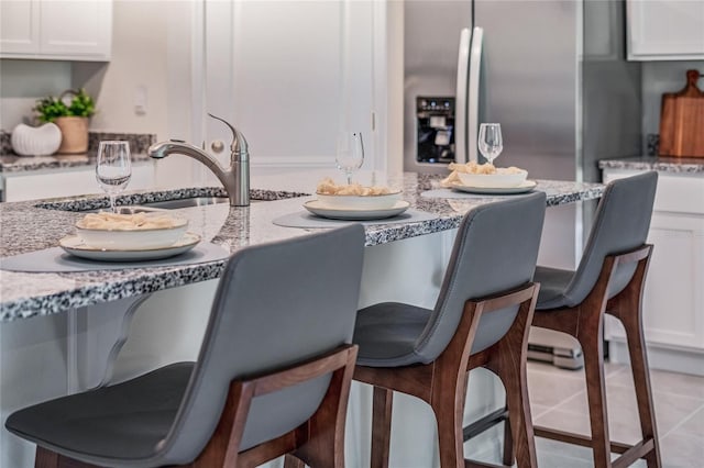 kitchen with light tile patterned floors, white cabinets, stainless steel fridge, and light stone countertops